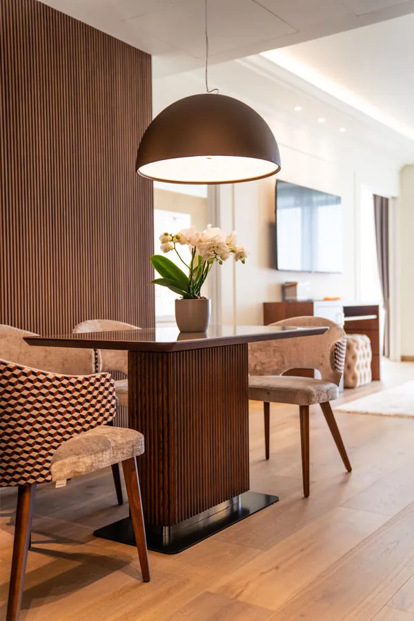 Hotel junior suite in style contemporaneo, tavolo con piano in ceramica e base cannettata, sedie contemporanee con gambe in legno e rivestimento bicolore.
